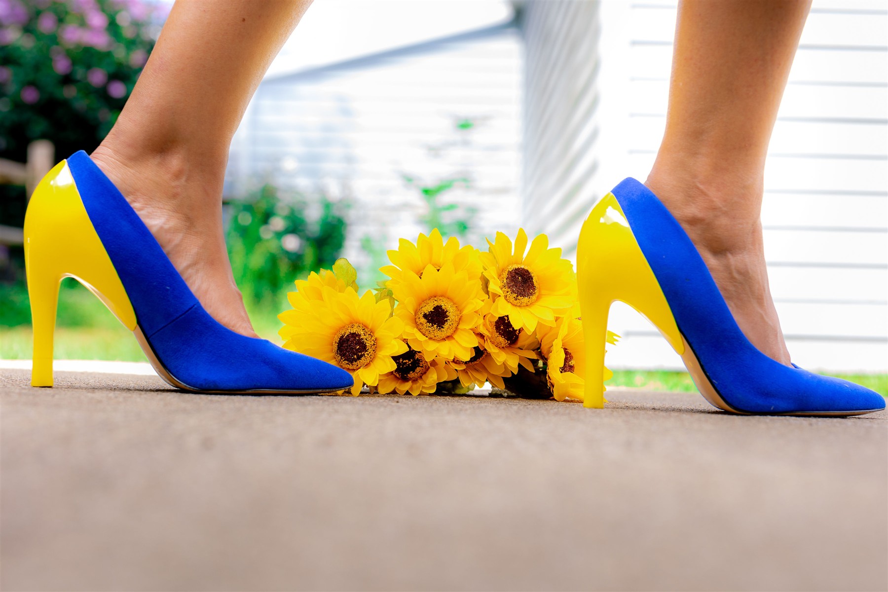 Blue slim high heels with yellow heel covers beside a bouquet of yellow flowers